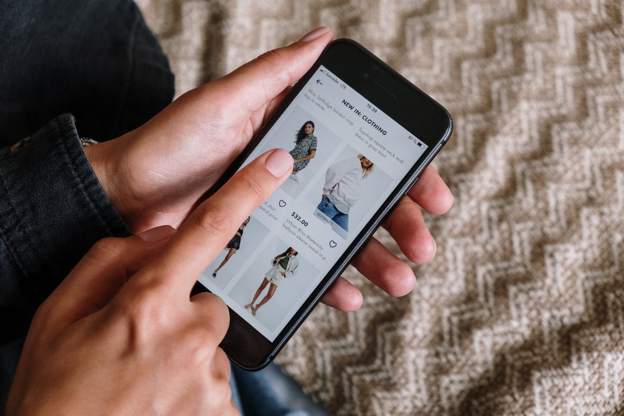 En person holder en smartphone og ser på tøjudvalg i en online butik, mens de navigerer med en finger på skærmen.