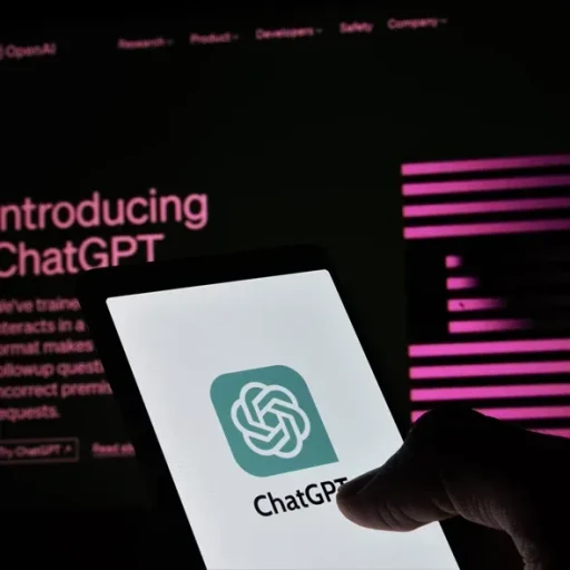 En hånd holder en smartphone, der viser ChatGPT-logoet, mens en online præsentation med teksten "Introducing ChatGPT" og en mørk baggrund kan ses i baggrunden.
