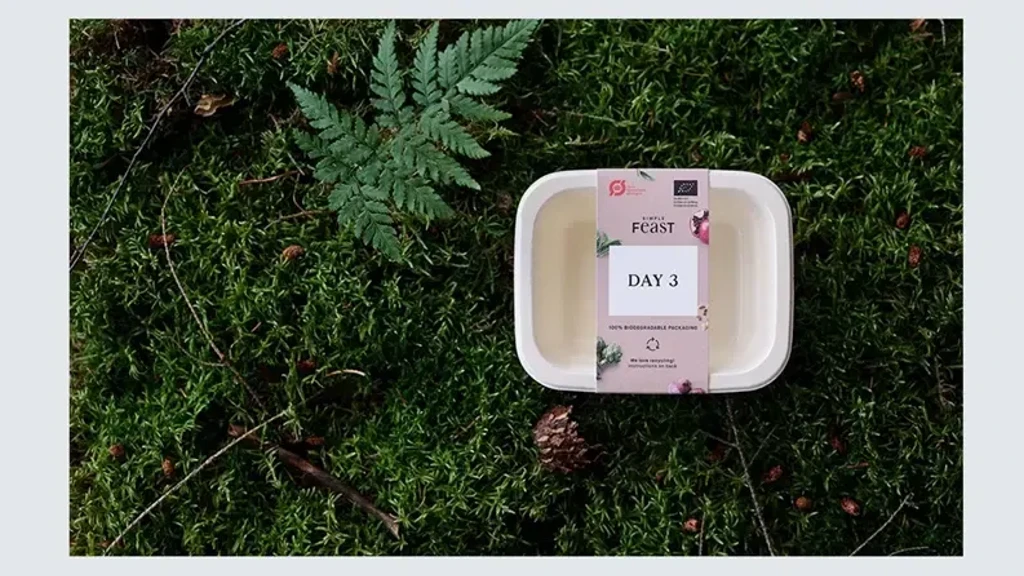 Beholder med label "DAY 3" på græsset, omgivet af enebær og bregner, der viser bæredygtig emballage.