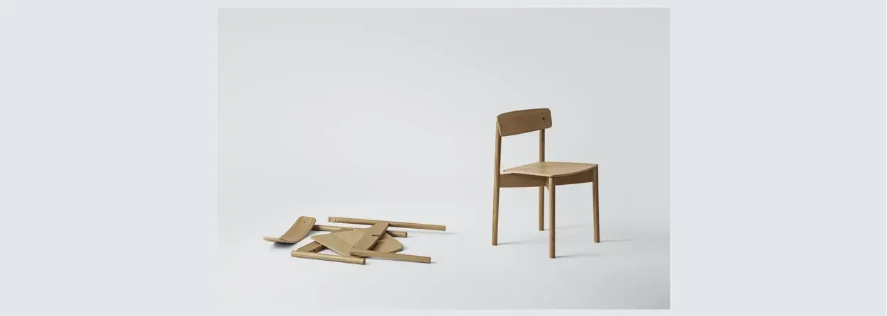 Et enkelt, moderne træstol står til højre, mens en bunke af adskilte stoledele ligger på venstre side, alt sammen på en hvid baggrund.
