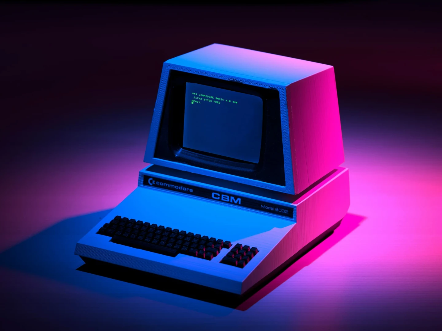 Billede af en retro Commodore CBM model 6032 computer med grøn tekst på en sort skærm, oplyst af blå og lilla lys, som fremhæver tastaturet og computerens karakteristiske design.
