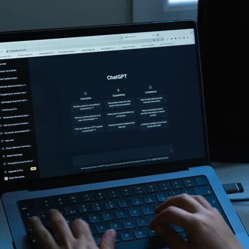 En person sidder ved en bærbar computer med en mørk skærm, der viser ChatGPTs interface med sektioner for eksempler, kapaciteter og begrænsninger.
