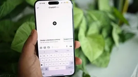 En person holder en smartphone med ChatGPT-appen åben, mens der ses grønne planter i baggrunden.