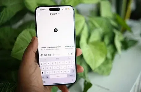 En person holder en smartphone med ChatGPT-appen åben, mens der ses grønne planter i baggrunden.