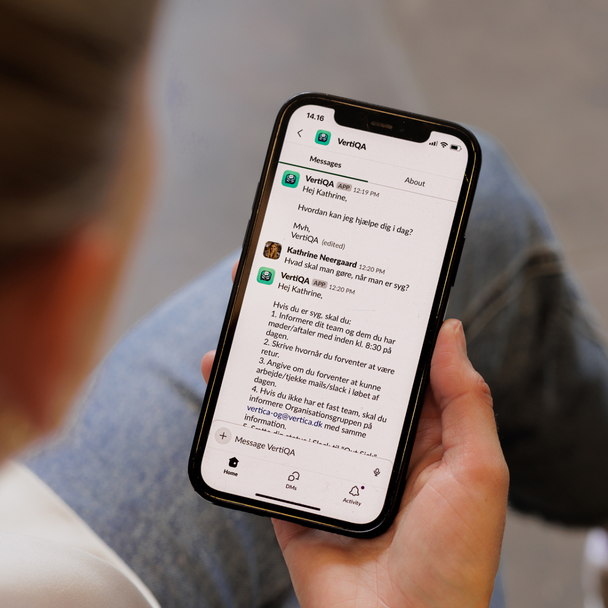 En person holder en smartphone, der viser en beskedudveksling i VertiQA-appen med en besked til "Kathrine" og svar om, hvordan man kan få hjælp. Skærmen viser detaljer om kontakten og behandlingsinstrukser.